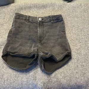 Svarta jeansshorts från H&M Divided - Snygga svarta jeansshorts från H&M Divided i storlek 36. Modellen har hög midja, klassiska fem fickor och råa kanter nedtill för en cool vibe. Perfekta för sommarens alla äventyr och passar till allt. Materialet är mjukt denim med lite stretch.