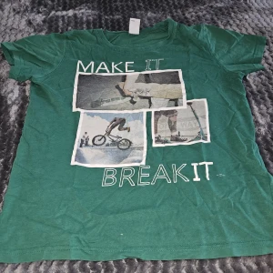 Grön t-shirt med BMX-tryck från Lindex - Cool grön t-shirt från Lindex med tryck i vitt och bilder på BMX och sparkcykel samt texten 'MAKE IT BREAK IT' på framsidan. Rund hals och korta ärmar, tillverkad i mjuk bomull. Perfekt för dig som gillar action och streetstyle.