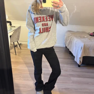 Grå hoodie med tryck - Säljer en grå hoodie med röd text 'WEEKEND AND CHILL' på bröstet. Tröjan har huva med snörning och en stor magficka. Perfekt för avslappnade dagar och har en loose passform. Materialet känns som mjuk bomull och polyester.