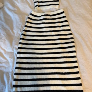 Randig stickad långkjol i svart och vitt & topp - Säljer en snygg stickad långkjol med horisontella svarta och vita ränder. Kjolen har en rak och enkel form som ger en chill vibe. Perfekt att matcha med en crop top för en cool look. Materialet är mjukt och ribbat, vilket gör den skön att bära.