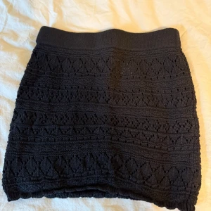 Svart stickad kortkjol med mönster - Supersöt svart stickad kortkjol med snyggt hålmönster och bred resår i midjan. Kjolen har en cool struktur och känns både trendig och bekväm. Perfekt att styla med en oversized tröja eller crop top.