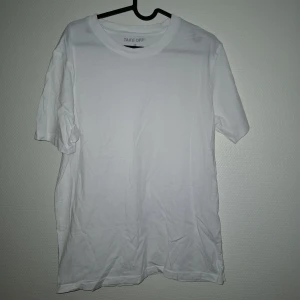 Vit t-shirt från Take Off i bomull - Klassisk vit t-shirt från Take Off i storlek M. Modellen har rund hals och korta ärmar, perfekt för en clean och enkel stil. Tillverkad i mjuk bomull som känns skön mot huden. Passformen är normal och t-shirten är helt utan mönster eller detaljer.