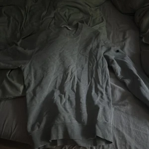 Grå sweatshirt från Stone Island - Grå långärmad sweatshirt från Stone Island med klassisk rund halsringning. Tröjan har en enkel och clean design utan tryck, tillverkad i mjuk bomull. Perfekt för dig som gillar streetwear och vill ha en stilren look. Skick 3/10. Finns logga också