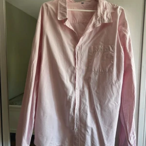 Ljusrosa skjorta med bröstficka - En stilren ljusrosa skjorta i bomull med klassisk krage och knäppning framtill. Skjortan har en bröstficka med knapp och långa ärmar. Perfekt för dig som gillar en clean och enkel look.