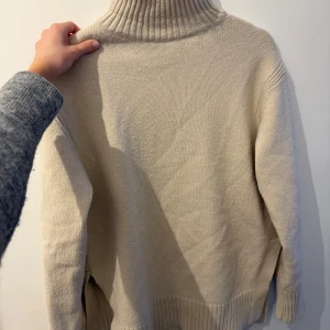 Beige stickad polotröja med slits - Säljer en oversized beige stickad polotröja med ribbad hög krage och breda muddar. Tröjan har långa ärmar och en snygg slits i sidan som ger en chill vibe. Perfekt till hösten🍂från hm⭐️⭐️