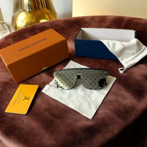 Louis Vuitton svarta monogram solglasögon - Snygga svarta solglasögon från Louis Vuitton med spegellins och ikoniskt LV-monogram över hela glaset. Sköldpaddsinspirerad, futuristisk form med breda skalmar där Louis Vuitton-loggan är ingraverad. Kommer med originalbox, fodral och putsduk.