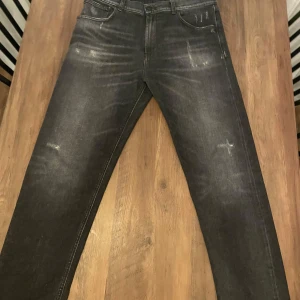 Svarta jeans från Dondup - Snygga svarta jeans från Dondup med slitna detaljer och tvättad look. Jeansen har en mörkgrå ton och är tillverkade i bomull med en skön passform. Perfekta för dig som gillar en avslappnad men stilren vibe.10/10 skick och alla slitningar är original.