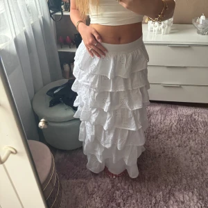 Vit långkjol med volanger och broderi från Gina Tricot  - Superfin vit långkjol med flera lager volanger och broderade blommor. Kjolen är i luftig bomull och har en romantisk känsla med sina broderade detaljer och vågiga kanter. Perfekt för dig som vill ha en boho-vibe och älskar flowiga plagg. Endast testad!
