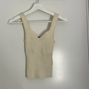 Ribbad beige linnetopp XS - Supersnygg ribbad linnetopp i beige med breda axelband och markerad v-ringning. Toppen är stickad och har en figurnära passform som framhäver siluetten. Perfekt att styla för en clean look. (Aldrig använd)