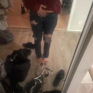 Mörkblå ripped jeans med straight fit - Säljer ett par mörkblå jeans med snygga slitningar och hål på båda benen. Modellen är straight fit och midwaist, med klassisk femficksdesign och dragkedjegylf. Perfekta för dig som gillar en edgy och avslappnad stil.