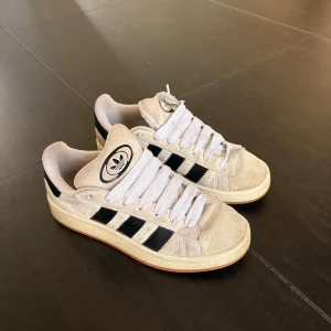 Adidas Campus sneakers i beige mocka - Snygga Adidas Campus sneakers i beige mocka med klassiska svarta ränder på sidorna och vit Adidas-logga på plösen. Skorna har vit snörning, rund tå och en gummisula i naturfärg. Använda några gånger och säljer pga använder inte längre. Pris kan diskuteras💸