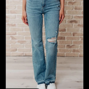 Blå bootcut jeans från Gina tricot - Låg/mid waist Bootcut jeans i ljusblå från Gina tricot, med slitningar och hål på ena knät. Jag är 165cm lång och byxorna når ner till golvet på mig. Lägg gärna ett bud☺️(har samma passform som byxorna på första bilden)