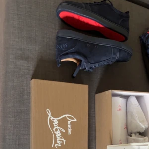 Mörkblå sneakers från Christian Louboutin - Exklusiva mörkblå sneakers från Christian Louboutin i mocka med den ikoniska röda sulan. Skorna har rund tå, snörning och en stilren design som sticker ut. Perfekta för dig som vill ha något unikt och lyxigt i garderoben.