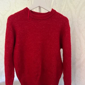 Röd stickad tröja från Pimkie - En klassisk röd stickad tröja från Pimkie med rund halsringning och långa ärmar. Tröjan har en enkel och tidlös design med ribbade muddar vid hals, ärmslut och nederkant. Perfekt för dig som gillar färg och vill ha en mysig baströja i garderoben.