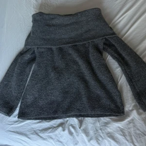 Mörkgrå stickad offshoulder-tröja H&M - Mysig mörkgrå stickad tröja från H&M i offshoulder-modell. Tröjan har långa ärmar och en bred krage som sitter snyggt över axlarna. Perfekt för dig som gillar en chill men ändå trendig look under kyliga dagar.