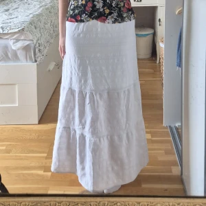 Vit långkjol med volangdetaljer - Vit långkjol med volangdetaljer och lätt struktur i tyget. Kjolen har en rak passform upptill och faller snyggt ner mot anklarna. Perfekt för varma dagar och enkel att styla. Den har en innerkjol så den är inte genomskinlig. Säljer då den inte används, använd några gånger. Hör gärna av dig vid frågor💕