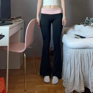 Svarta bootcut byxor med rosa midja - Snygga svarta bootcut byxor med bred rosa midja som kan vikas ner. Stretchigt material. Xs men skulle säga att de passar xxs 