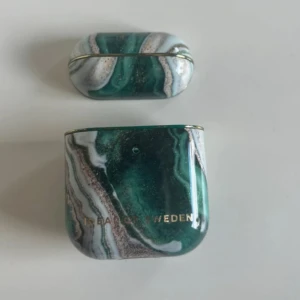 Grön marmorerad AirPods-fodral från Ideal of Sweden - Snyggt AirPods-fodral från Ideal of Sweden med marmorerat mönster i grönt, vitt och inslag av guld. Fodralet har en glansig finish och detaljer i guld, perfekt för att ge dina hörlurar en unik och trendig look.