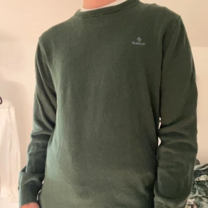 Mörkgrön stickad tröja från GANT - Mörkgrön stickad tröja från GANT med diskret logga på bröstet. Klassisk rund halsringning och långa ärmar. Perfekt för dig som gillar stilrena och tidlösa plagg. Skön passform och enkel att matcha med jeans. Pris kan diskuteras och förhandlas. 