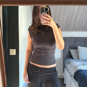 Grå tight ärmlös topp - Säljer en grå, figurnära topp med hög hals och ärmlös design. Toppens material är stretchigt och följsamt, vilket ger en snygg siluett. Perfekt att styla med jeans eller kjol för en clean look. Passar storlek xs/s