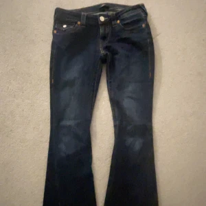 True Religion Joey Low Rise Flare jeans - Mörkblå jeans från True Religion, modell Joey Low Rise Flare. Snygg bootcut med låg midja och klassiska kontrastsömmar. Bakfickor med lock och knapp, tillverkade i jeansmaterial. Perfekta för dig som gillar retrovibbar och markerad siluett. Lite slitna på botten av jeansen men inget man tänker på 