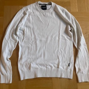 Vit stickad tröja från Only & Sons - Snygg vit stickad tröja från Only & Sons med rund halsringning och långa ärmar. Tröjan har ribbade muddar vid ärmslut och nederkant, perfekt för en clean och stilren look. Passar till jeans eller chinos för en enkel outfit.