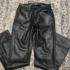 Svarta skinnbyxor från BikBok - Snygga svarta byxor i skinnimitation från BikBok. De har raka ben, klassisk femficksdesign och bälteshällor. Perfekta för dig som vill ha en edgy look med lite glansig finish. Passar till allt från sneakers till boots.