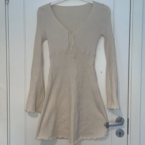 Beige ribbad klänning från SHEIN - Supersöt beige ribbad klänning från SHEIN i storlek S. Den har långärmade trumpetärmar med vågig kant, v-ringning med snörning framtill och en kort, figurnära passform. Perfekt för dig som gillar stilrena och mjuka plagg med lite extra detalj.