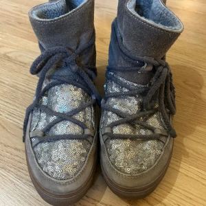 Grå glittriga boots från Inuikii - Snygga grå boots från Inuikii med glittriga paljetter på ovandelen och mjukt mocka runt skaftet. Skorna har grova snören som går runt hela skon och en varm, fodrad insida. Fodringen är avskavd i skon, sista bilden, så inte lika fluffiga som nyköpta 
