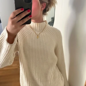 Ribbad polotröja från Gina Tricot - Säljer en krämvit ribbad polotröja från Gina Tricot med hög hals och långa ärmar. Tröjan är stickad i mjukt material och har en loose passform som ger en chill vibe. Perfekt att styla med jeans eller kjol för en enkel look.