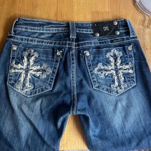 Miss Me jeans med broderade fickor - y2k - Säljer ett par blå Miss Me jeans med snygga broderade kors på bakfickorna och dekorativa nitar. Jeansen har kontrastsömmar, klassisk femficksdesign och bootcut passform. Materialet är jeans med stretch för extra komfort.