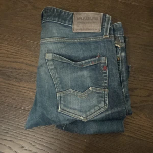 Replay jeans - Säljer ett par Replay Waitom jeans i klassisk blå tvätt med snygga slitningar och detaljerade sömmar. Jeansen har raka ben, normal passform och coola knappar med Replay-logga. Perfekta för dig som gillar en tidlös och avslappnad stil. Kom med bud och frågor! 