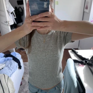 Kortärmad stickad topp - Säljer en ljusgrå stickad topp från Filippa K som har korta ärmar. Toppen har en enkel och stilren design med diskret glittrig effekt i materialet. Perfekt att styla med jeans eller kjol för en clean look