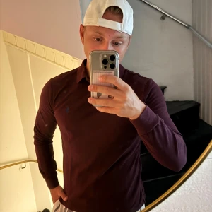 Vinröd pikétröja från Polo Ralph Lauren - Säljer en vinröd långärmad pikétröja från Polo Ralph Lauren i custom fit. Tröjan har klassisk krage, knappar vid halsen och den ikoniska blå loggan broderad på bröstet. Perfekt för dig som gillar stilren och tidlös design.