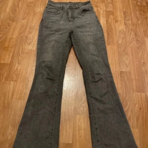 Mörkgrå bootcut jeans - Snygga mörkgrå jeans med bootcut-modell och klassisk femficksdesign. Jeansen har hög midja och är tillverkade i ett mjukt denimtyg som ger en skön passform. Perfekta för dig som gillar en retrovibe och vill ha ett par jeans som sticker ut.