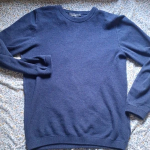 Mörkblå stickad tröja Dressmann M - Snygg mörkblå stickad tröja från Dressmann i storlek M. Tröjan har rund hals, ribbade muddar vid ärmslut och nederkant samt långärmad passform. Perfekt för dig som gillar enkel och stilren look. Materialet är mjukt och skönt, tillverkat av bomull. Najs för lägga till något på outfiten och passar med skjortor. Lågt pris däröver pga av it användning längre