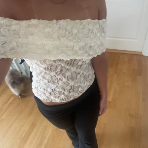 Vit offshoulder spets tubtopp - Superfin vit axelbandslös tubtopp med offshoulder-design och spetsdetaljer. Toppen har 3D-blommor upptill och är croppad med figurnära passform. Aldrig använd.