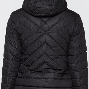 Svart quiltad pufferjacka med huva - Svart pufferjacka med snyggt quiltat mönster och huva. Jackan har knappar framtill, två fickor med lock och dragsko i huvan. Perfekt för kalla dagar och riktigt skön att bära. Passformen är normal och jackan har långa ärmar.