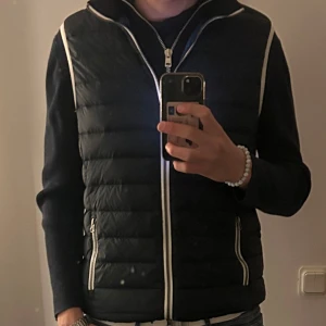 Marinblå East West dunväst med vita detaljer - Snygg marinblå dunväst och vita kantdetaljer. Perfekt att slänga över en hoodie. 