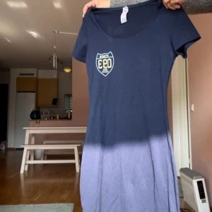 Mörkblå t-shirtklänning T.summer - Mörkblå t-shirtklänning från T.summer med tryck på bröstet och ryggen. Modellen är figurnära med rund halsringning och korta ärmar. Skön och enkel stil, perfekt för en avslappnad look. Designad i Korea.