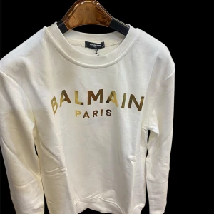 Vit sweatshirt  - Vit sweatshirt med guldig logga framtill. Tröjan har rund halsringning och långa ärmar. Tillverkad i mjuk bomull för en skön och avslappnad look. Perfekt för dig som gillar stilrena och exklusiva plagg med statement-tryck.