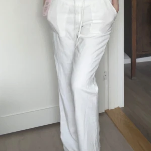 Helt oanvända, vita linnebyxor med snörning från Nelly - Snygga vita linnebyxor från Nelly i modell med låg midja och raka, lite loose ben. Byxorna har bred resår i midjan, snörning och stora fickor framtill. Helt oanvända då de inte kommit till användning! Ordinarie pris: 499 kr🤍