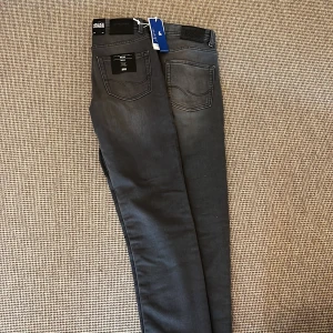 Jack&jones jeans grå - Snygga grå jeans från Jack & Jones i storlek 158 (13Y). Jeansen har en klassisk femficksmodell, svarta detaljer och en lätt tvättad look. Perfekta för dig som gillar en stilren och avslappnad vibe.
