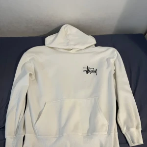 Vit Stüssy hoodie - Vit hoodie från Stüssy med svart logga på bröstet och stor blå tärningsgrafik på ryggen. Äkta fast använd så blir billigare. Äkta och i bra skick. Storlek: M (pris kan diskuteras)