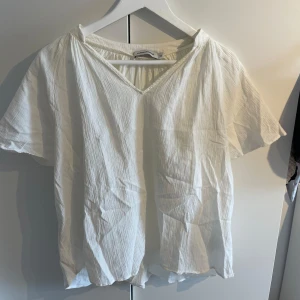 Vit v-ringad blus Carin Wester - Luftig vit blus från Carin Wester i storlek 36. Blusen har v-ringning, korta ärmar och är gjord i ett lätt, krinklat tyg som ger en avslappnad känsla. Perfekt till jeans eller kjol för en fräsch look.