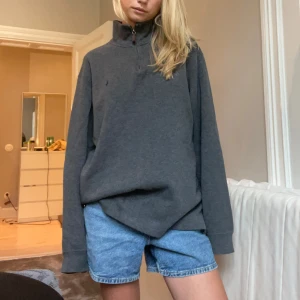 Grå half zip tröja från Ralph Lauren - Mörkgrå långärmad tröja från Ralph Lauren med half zip och hög krage. Oversized passform och diskret broderad logga på bröstet. Tillverkad i mjuk bomull, perfekt för chill dagar eller när du vill ha en clean look.