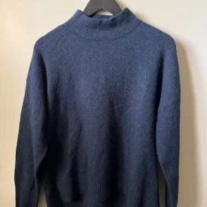 Mörkblå stickad polotröja - En mörkblå stickad polotröja med medel krage och långa ärmar. Den är använd ca 5 gånger och tvättad ca 2 gånger. Annars i bra skick.