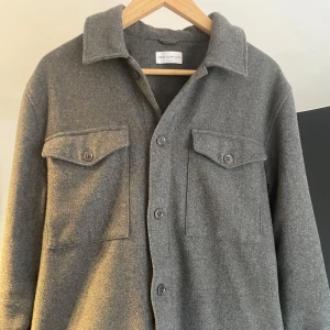 Grå overshirt från These Glory Days - Säljer en stilren grå overshirt från These Glory Days. Det är en lite tjockare overshirt , gjord av ull men passar perfekt till höst,vinter och våren. Nypris på denna är 1400, hör av er vid frågor