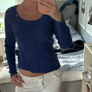 Mörkblå ribbad kofta med knappar - Säljer en mörkblå ribbad kofta med långa ärmar och rund halsringning. Koftan har knappar hela vägen framtill och är i en figurnära passform. Liten i storlek.