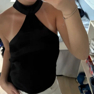 Svart halterneck topp i satin - Säljer en svart halterneck topp i glansigt satin material. Säljer då den inte kommer till användning, har använt 2 gånger annars.